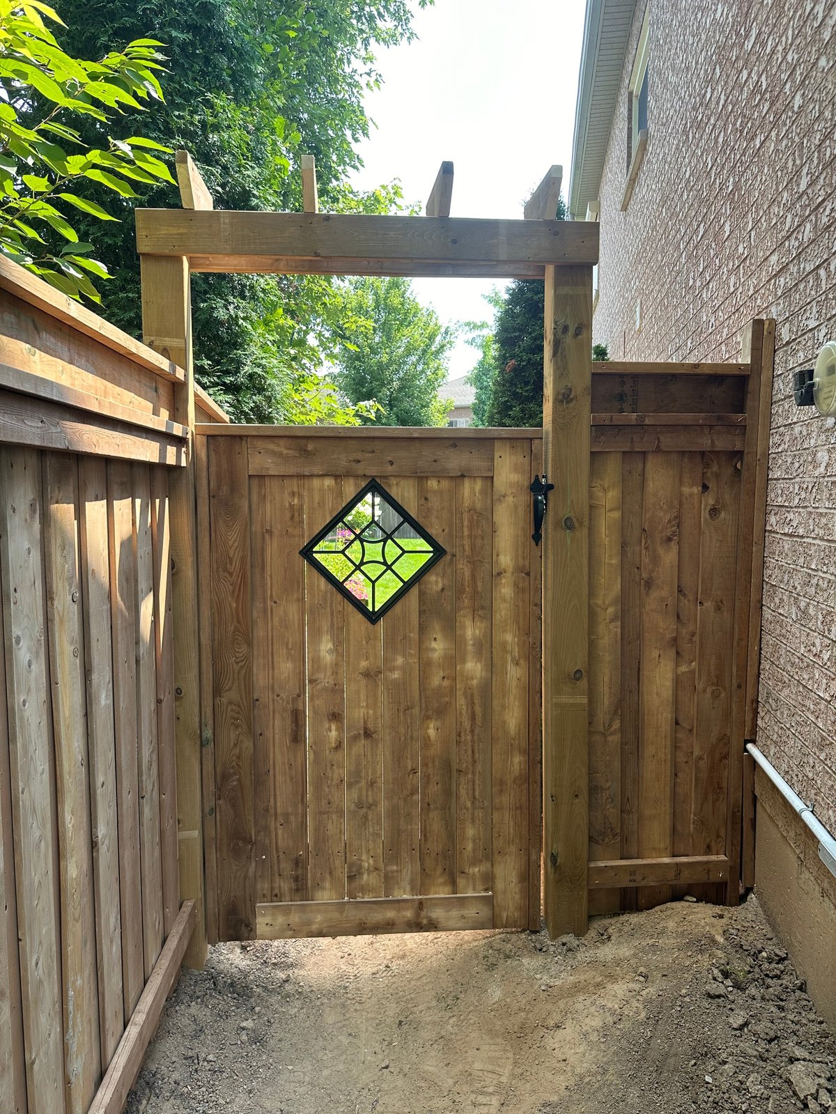 Wooden garden gate with diamond-shaped window, attached to fence and brick house exterior