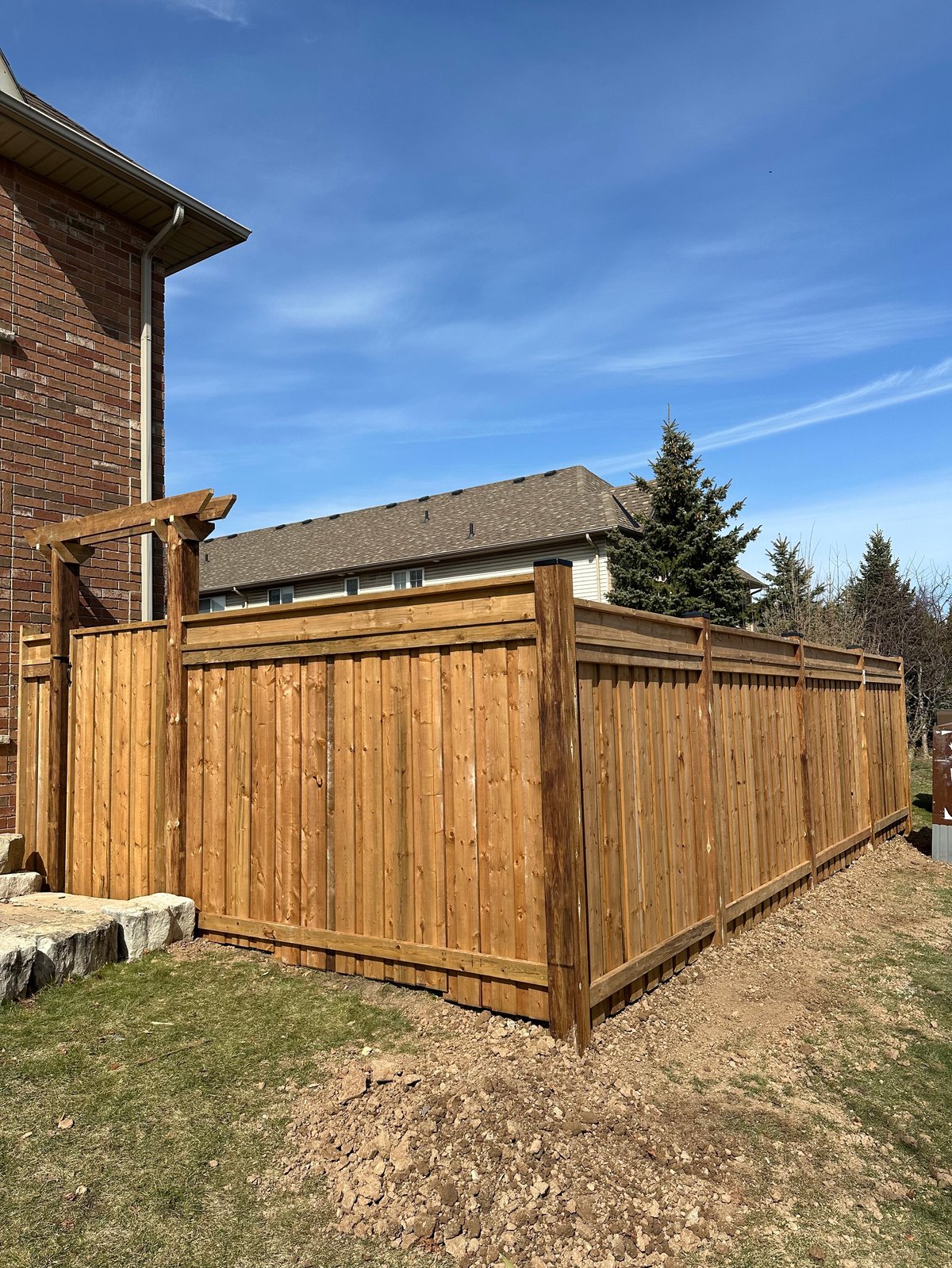 Wooden privacy fence surrounding a patio area next to a brick house with cedar trees in background