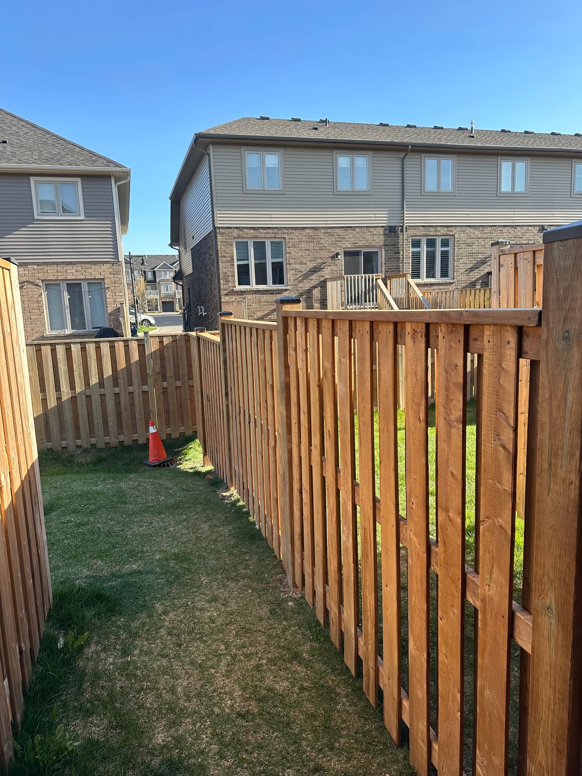 Narrow fenced backyard between residential houses with wooden fence and fire hydrant on green lawn