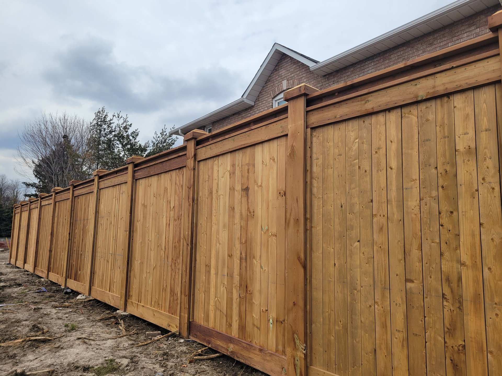 Long wooden privacy fence with vertical boards and metal posts against cloudy sky and bare trees
