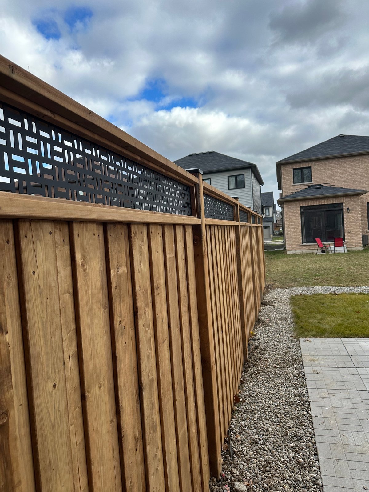 Wooden fence with decorative metal lattice screen alongside a brick house and neighboring homes in a residential area